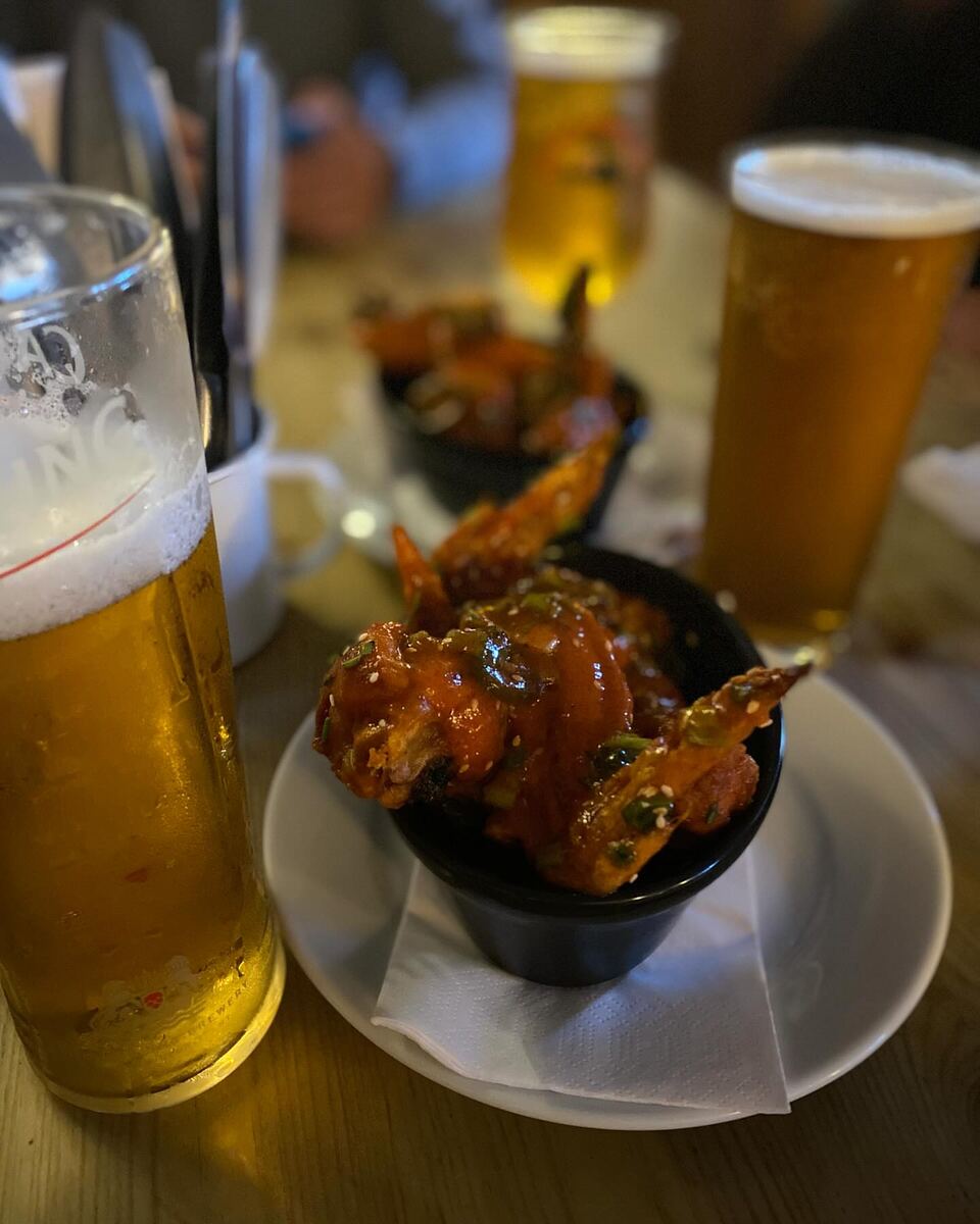 Two pints of lager beside a bowl of sticky chicken wings